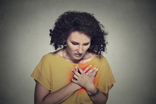 sick middle aged woman with heart attack, pain, health problem holding touching her chest colored in red with hands isolated on gray wall background. Human face expression
